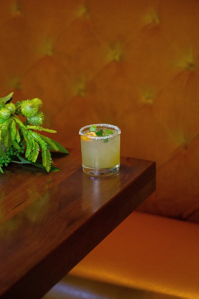 Salted yellow-green cocktail with citrus and herbs on dark wood.