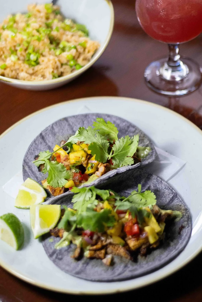 Two dark tacos with mango salsa, cilantro, and lime wedges.