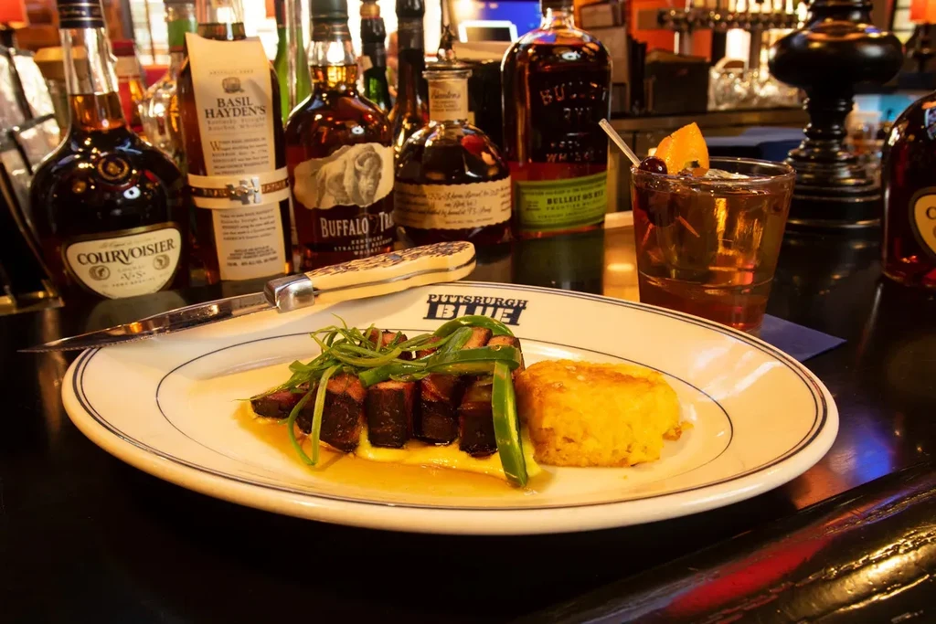 Seared meat, yellow sauce, polenta, and Old Fashioned at a bar.