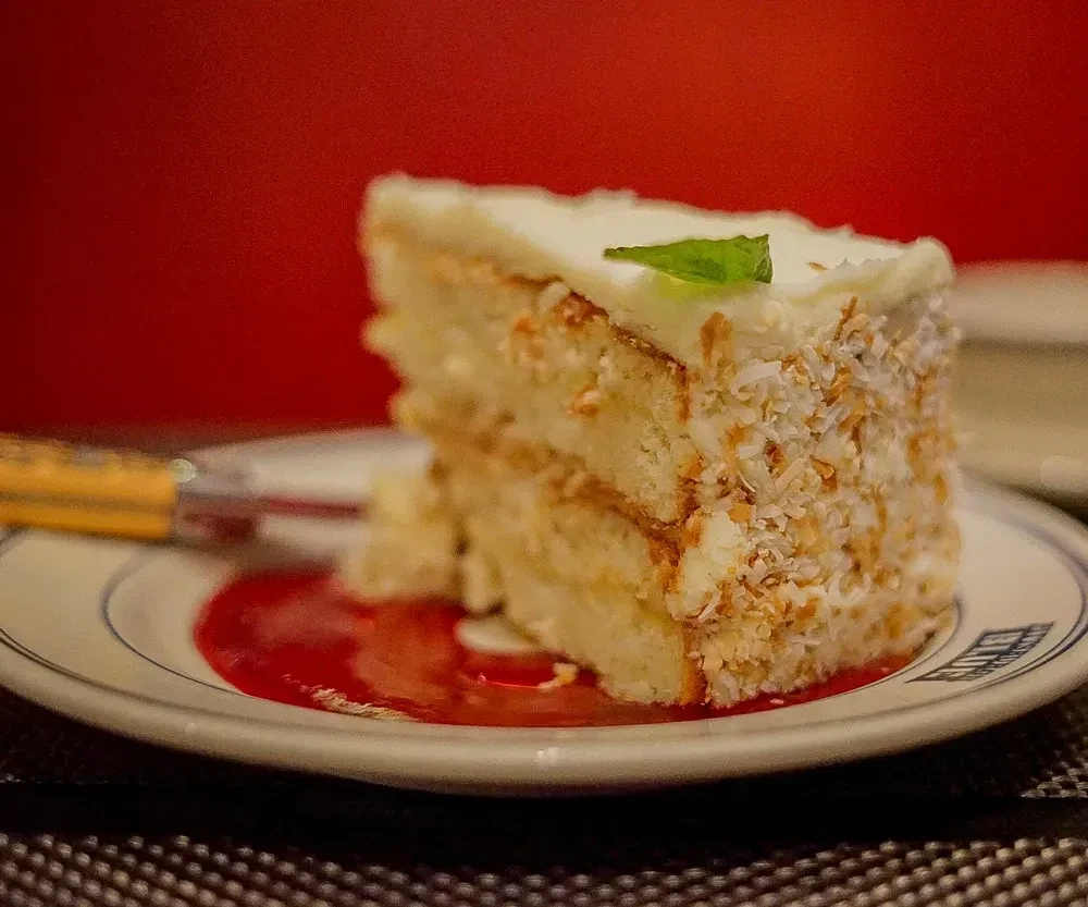 Slice of coconut layered cake with caramel, mint, and berry sauce.