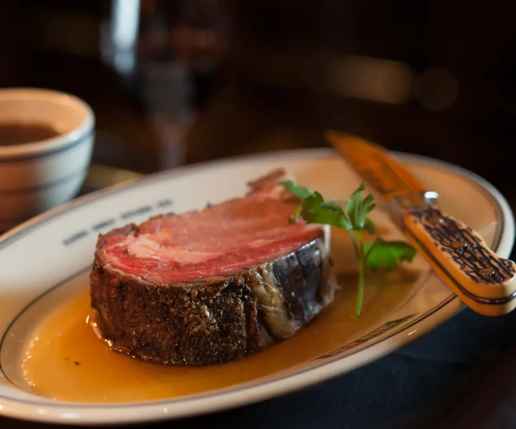 Close-up of medium-rare roasted meat, jus, parsley, and ornate knife.