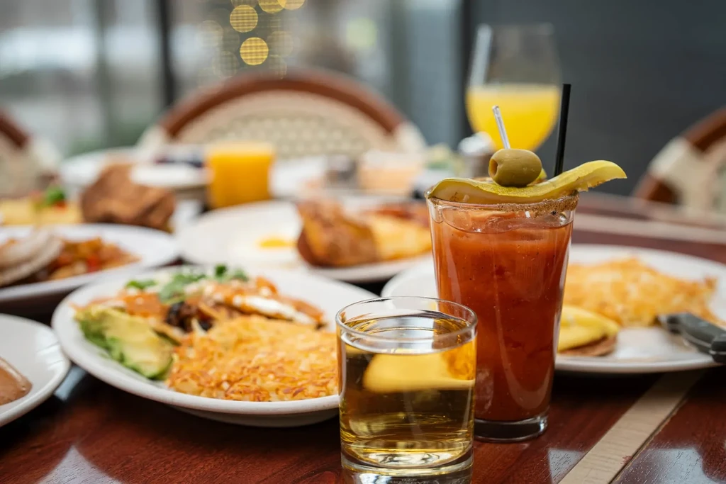 Restaurant brunch table with cocktails, hash browns, and avocado egg dish.