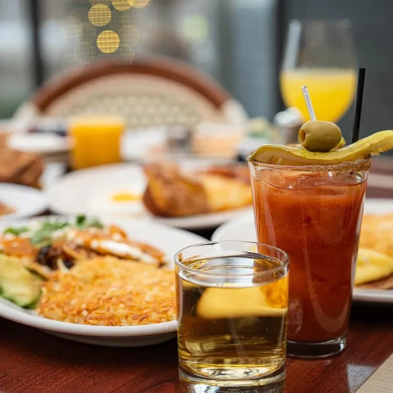Breakfast table with Bloody Mary, shot glass, hash browns, and eggs.