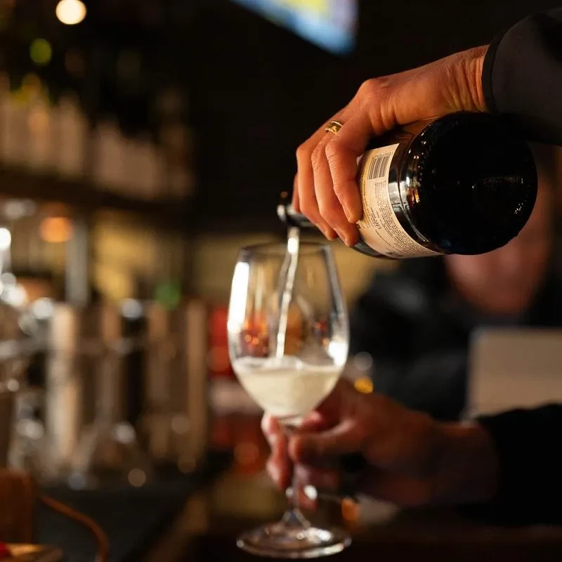 Hand with ring pours light liquid from dark bottle into glass.