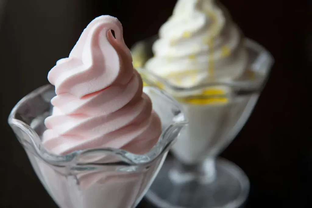 Two soft-serve desserts: pink in front, white with yellow drizzle behind.