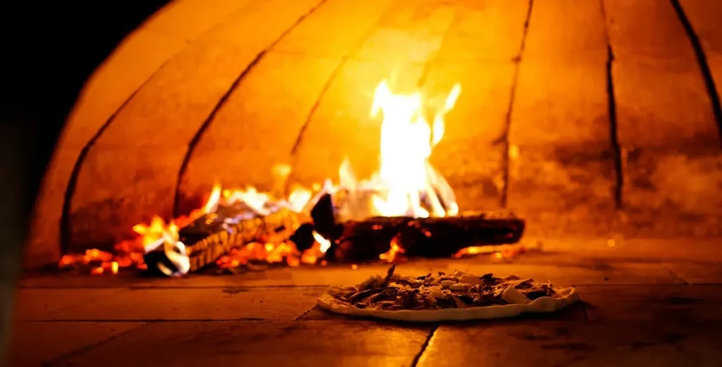 Raw pizza inside a wood-fired oven with blazing logs.