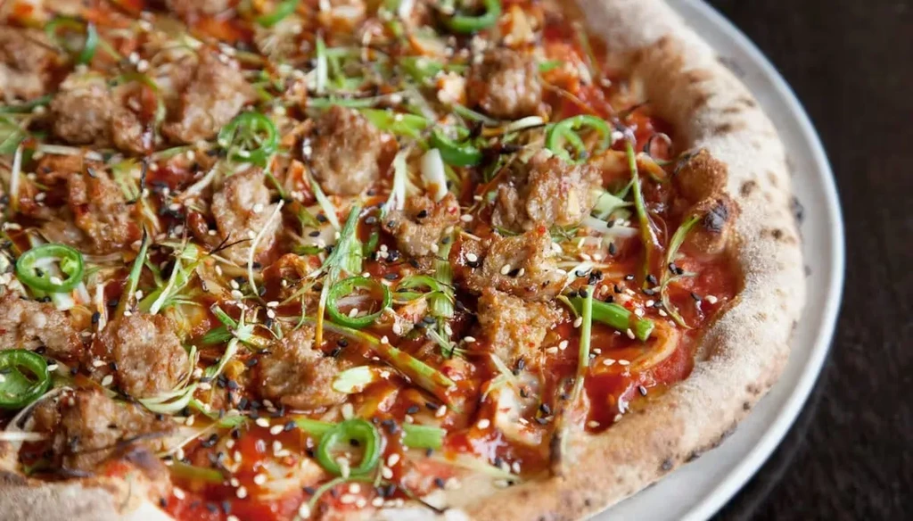 Wood-fired pizza with sausage, jalapeños, scallions, sesame, and a dark sauce.