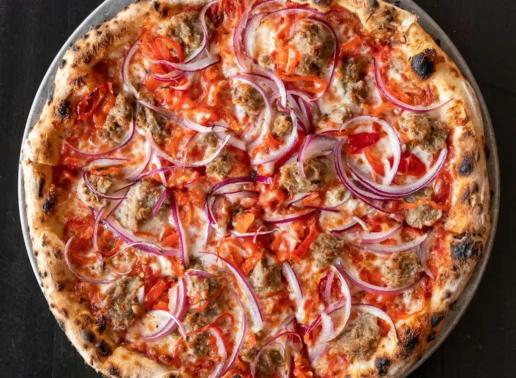 Freshly baked pizza with sausage, onion, and peppers on a pan.
