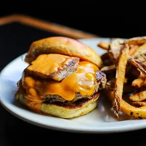 Burger with melted cheese, crispy topping, and fries on a plate.