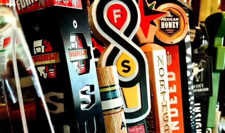 Close-up of diverse branded beer tap handles at a bar.