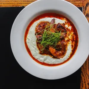 Plated shrimp and grits with sauce and green herbs in a white bowl.