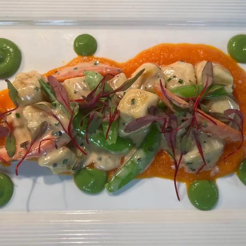 Plated gnocchi, snap peas, orange vegetables with two vibrant sauces.