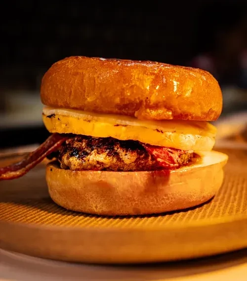 Close-up of a burger with char-grilled patty, bacon, thick topping, and sauce.