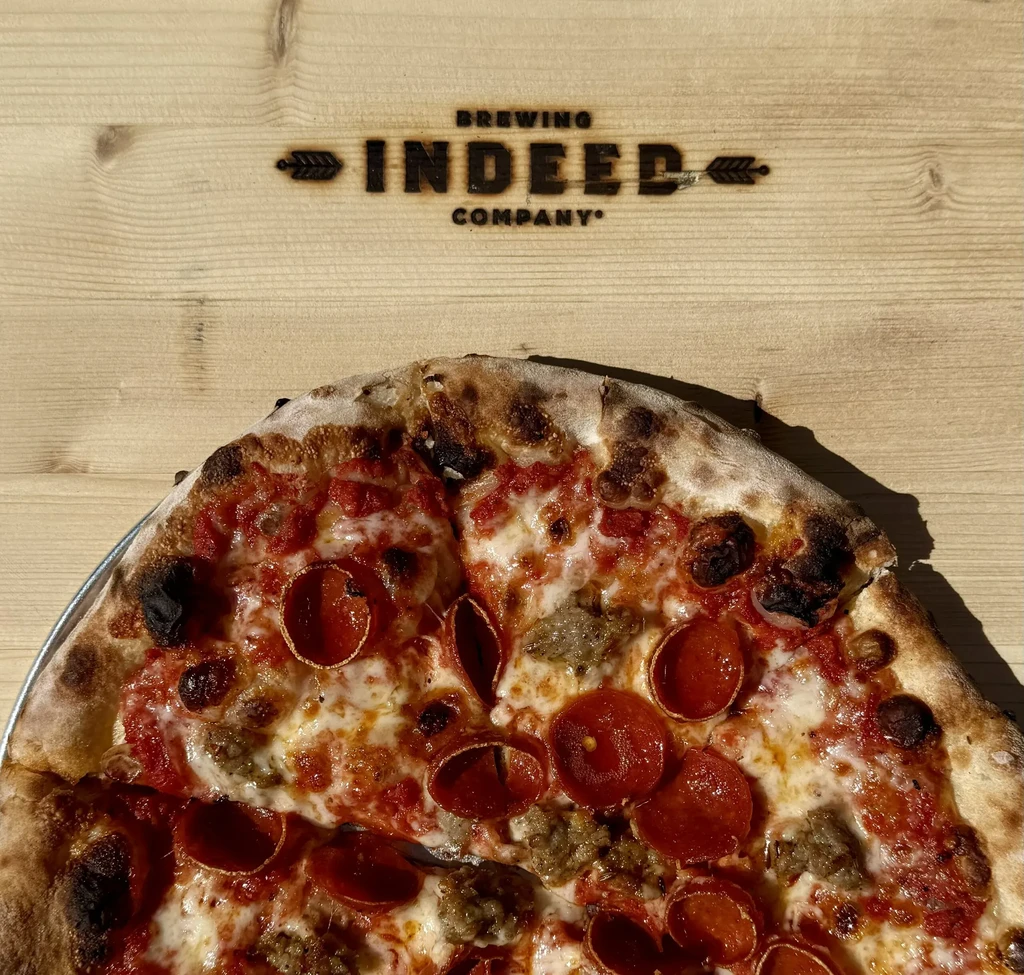 Partially eaten pepperoni and sausage pizza on a branded wooden surface.