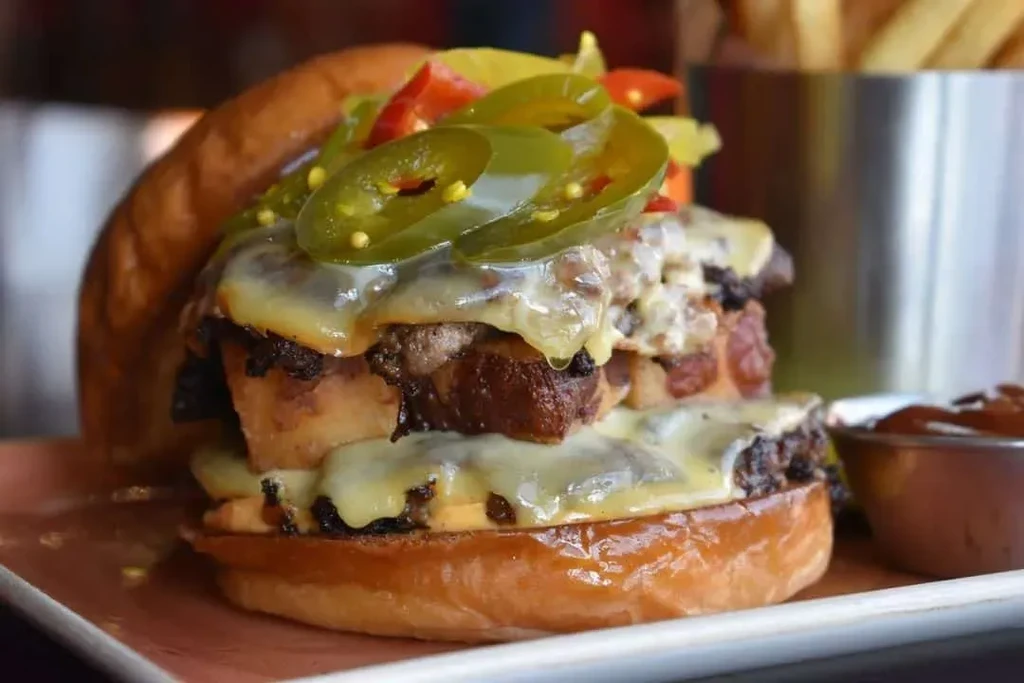 Gourmet burger with melted cheese, stacked meat patties, and jalapeños.