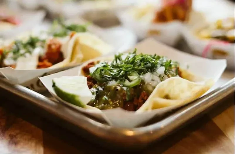Corn tortilla taco topped with green salsa, onions, cilantro, and lime.
