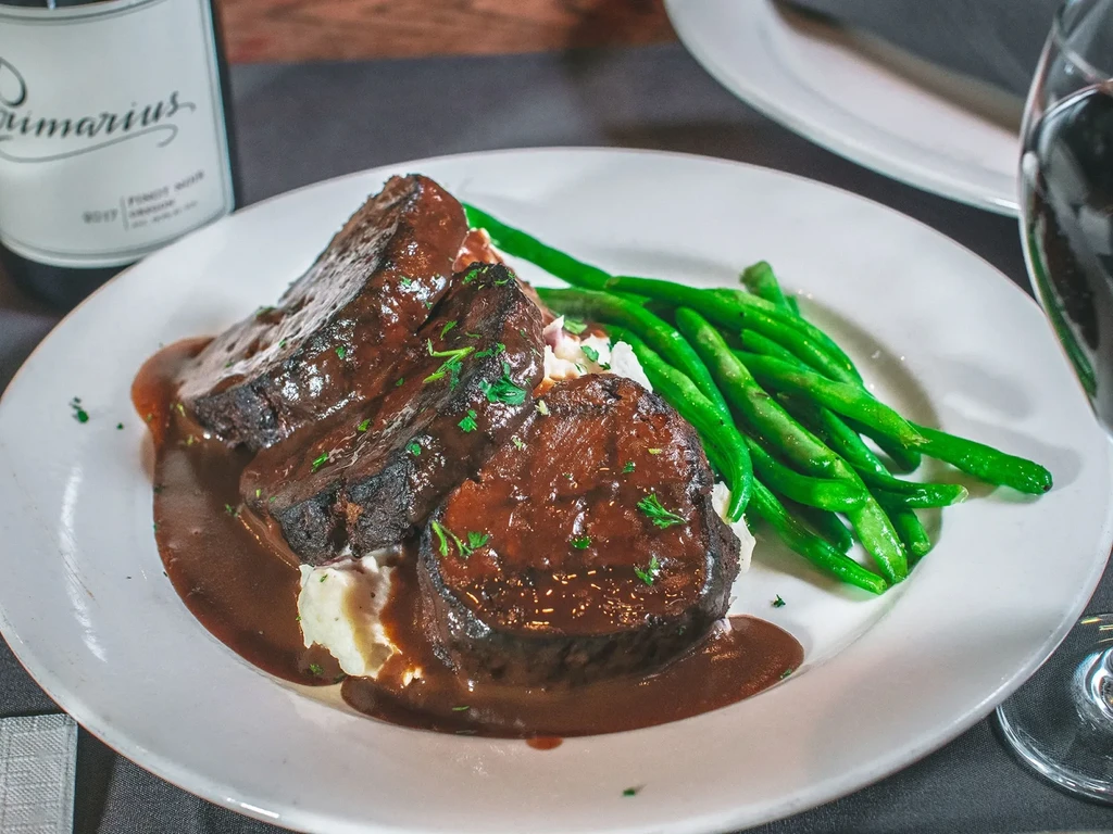 Slow-cooked meat with gravy, mashed potatoes, green beans, and wine.