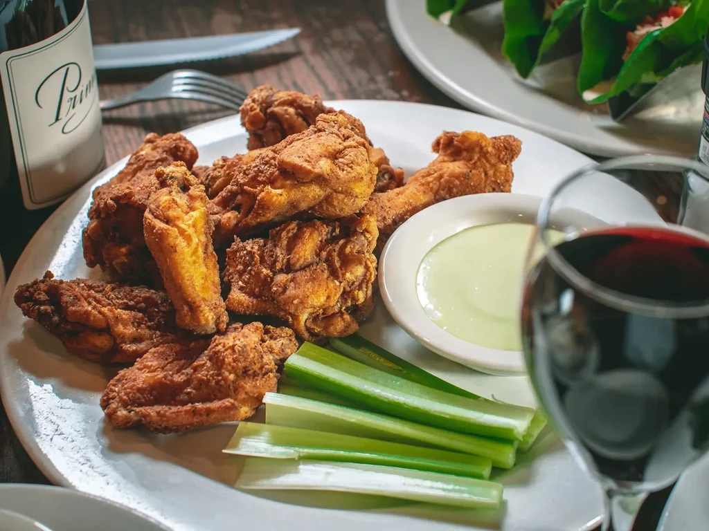 Crispy golden-brown fried chicken wings, green dipping sauce, and celery.