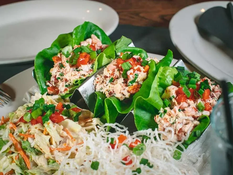 Three lettuce wraps, coleslaw, and vermicelli on a white plate.