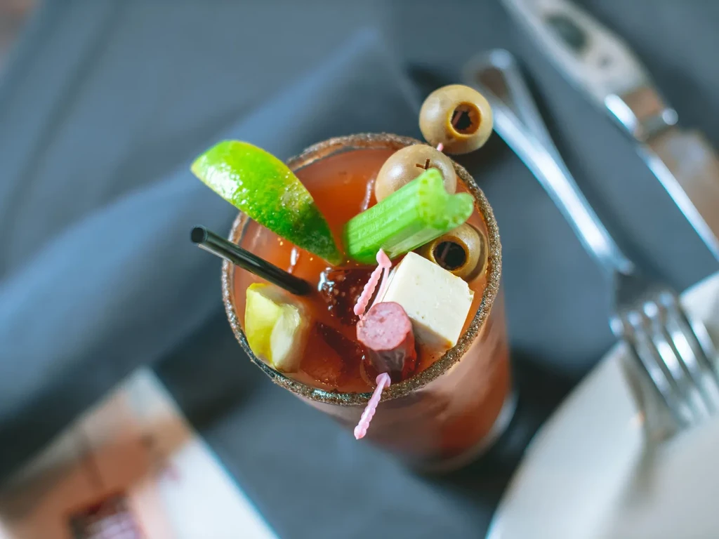 Richly garnished Bloody Mary cocktail with lime, celery, olives, cheese, and sausage.