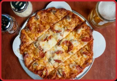 Square-cut pizza, beer, Parmesan, and red pepper flakes on a table.