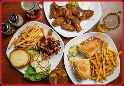 Top-down view: chicken wings, burger, sandwich, fries, and drinks on a table.