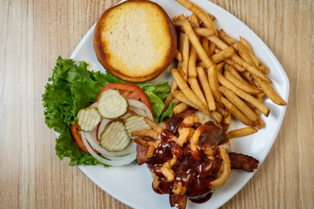Overhead deconstructed burger with bacon, cheese, separate toppings, and french fries.