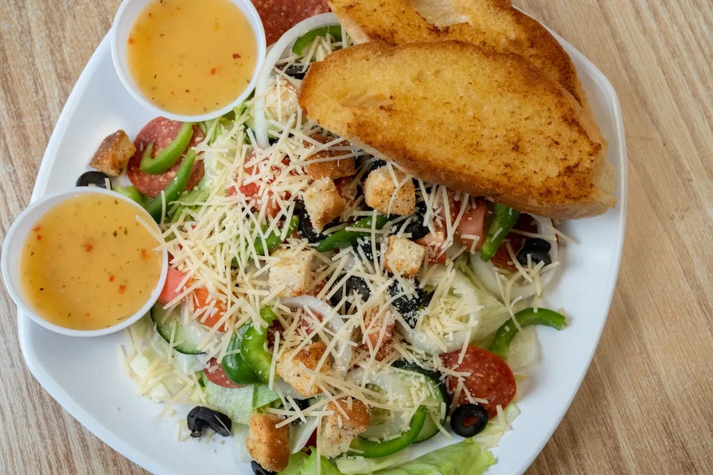 Colorful chef salad with pepperoni, cheese, vegetables, garlic bread, and dressing.