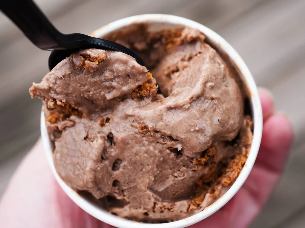 Spoon scooping chunky chocolate ice cream from a white cup.