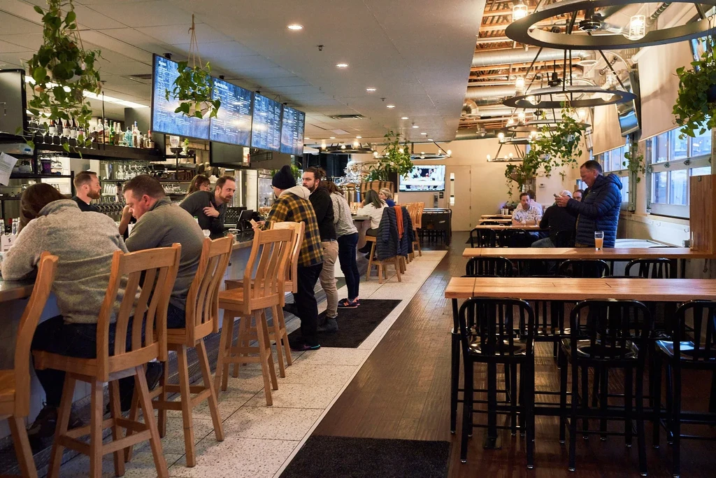 Modern bar interior with long counter, customers, and industrial decor.