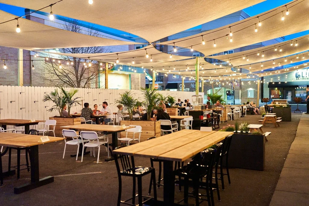 Dusk restaurant patio with sail canopies, string lights, and seated guests.