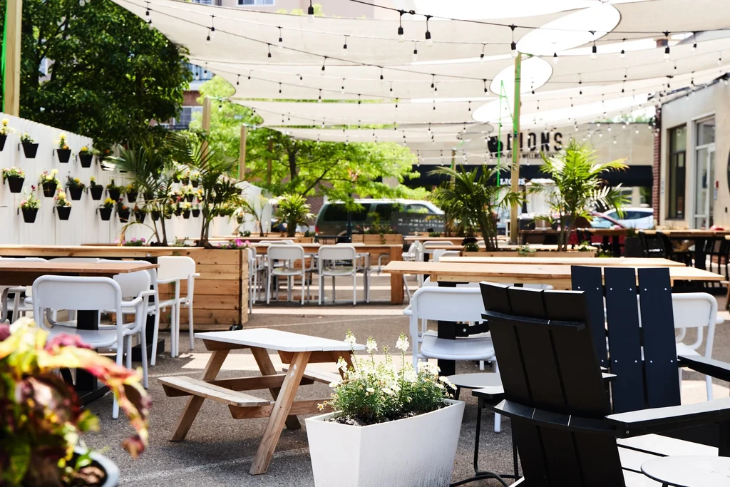 Sunny outdoor patio with diverse seating, shade sails, and vibrant plants.