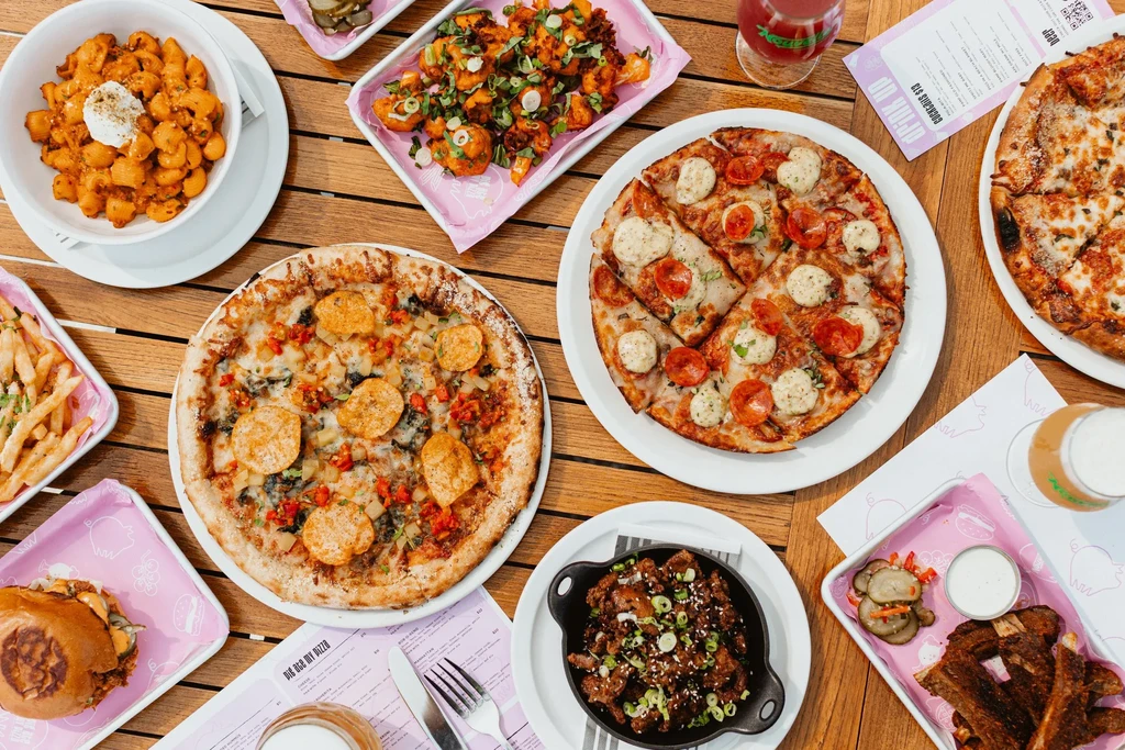 Overhead view of a wooden table with pizzas, burgers, ribs, and drinks.