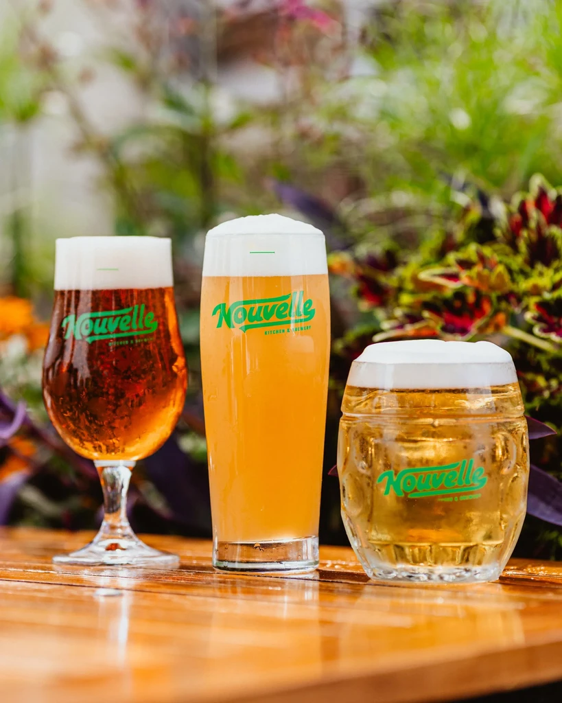 Three different beers with logos on a rustic wooden table outdoors.