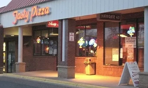 Lit-up exterior of Tasty Pizza and Hangar 45 storefronts at dusk.