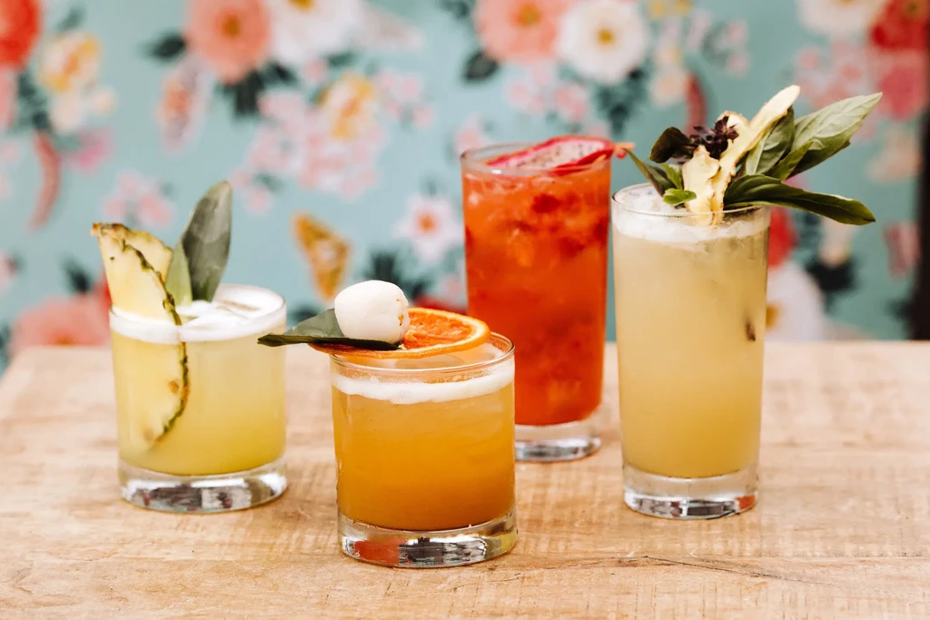 Four distinct, garnished cocktails on a light wooden table.