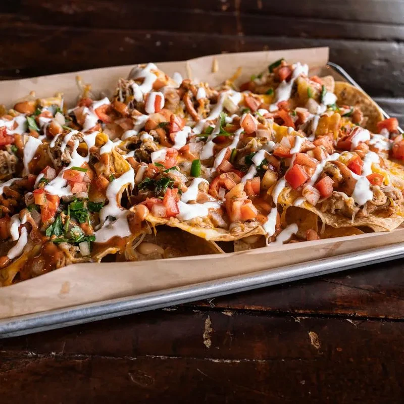 Tray of loaded nachos with melted cheese, pulled meat, tomatoes, and sour cream.