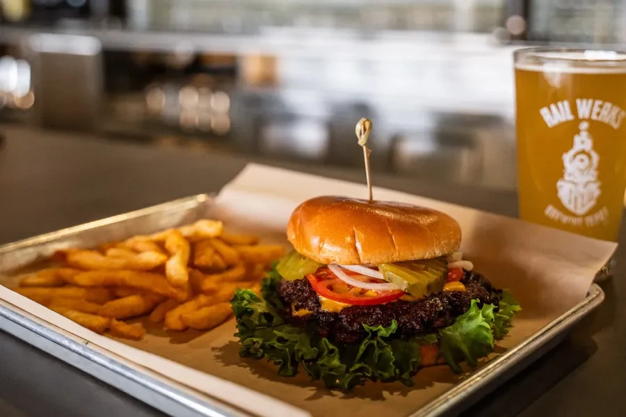 Close-up of a burger, fries, and RAIL WERKS beer on a tray.