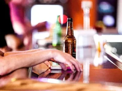 Hands and a brown beer bottle on a glossy bar counter.