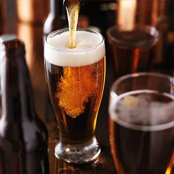 Golden beer pours into a clear glass, creating a foamy head.