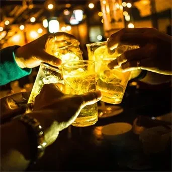 Multiple hands clinking glasses filled with glowing golden drinks.