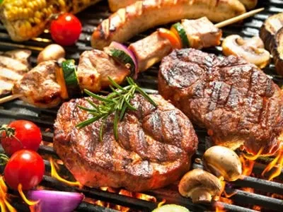 Grilled steaks, meat skewers, corn, and vegetables cooking on a barbecue.