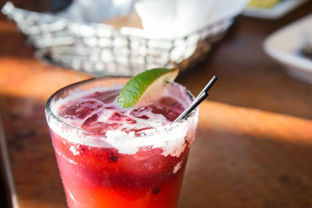 Red cocktail with salted rim, lime, ice, and black straws.