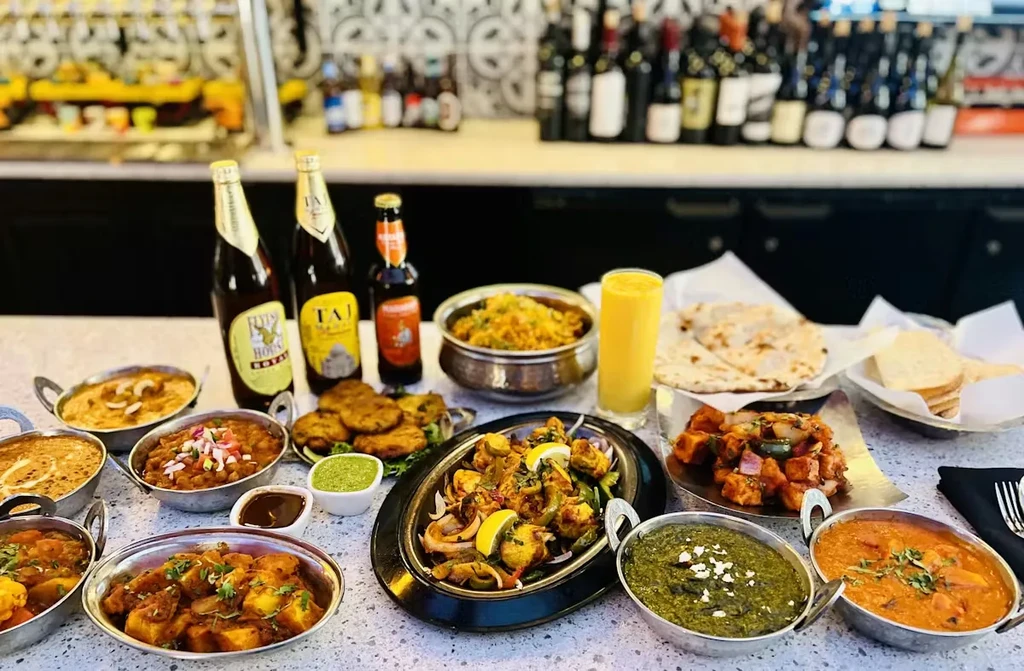 Indian food spread: curries, biryani, naan, mango lassi, and bottled beers.
