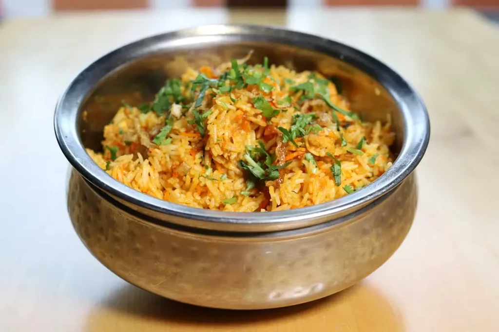 Close-up of orange-yellow spiced rice with cilantro in a metal bowl.