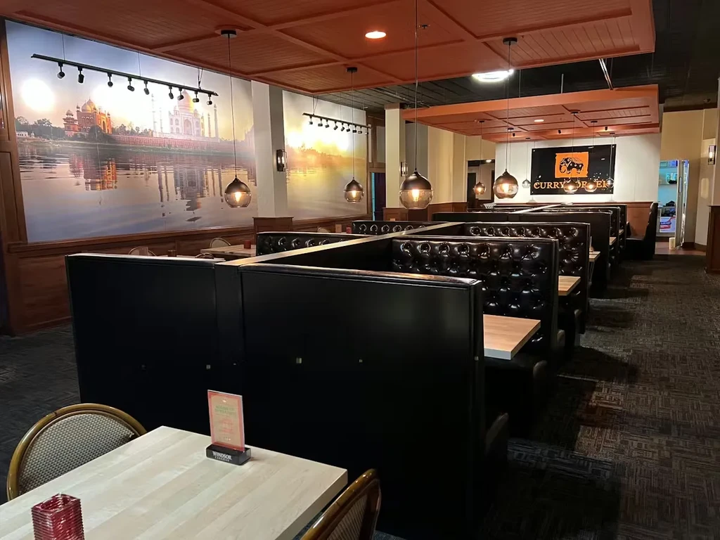 Empty Indian restaurant interior with booth seating and Taj Mahal mural.