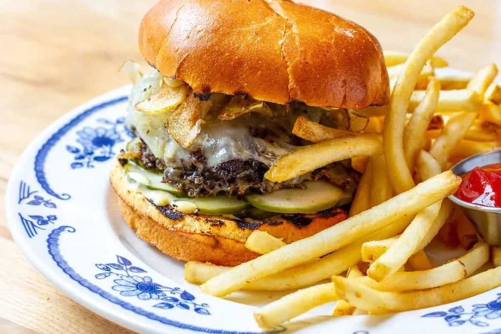 Gourmet burger, golden fries, and ketchup on a blue floral plate.