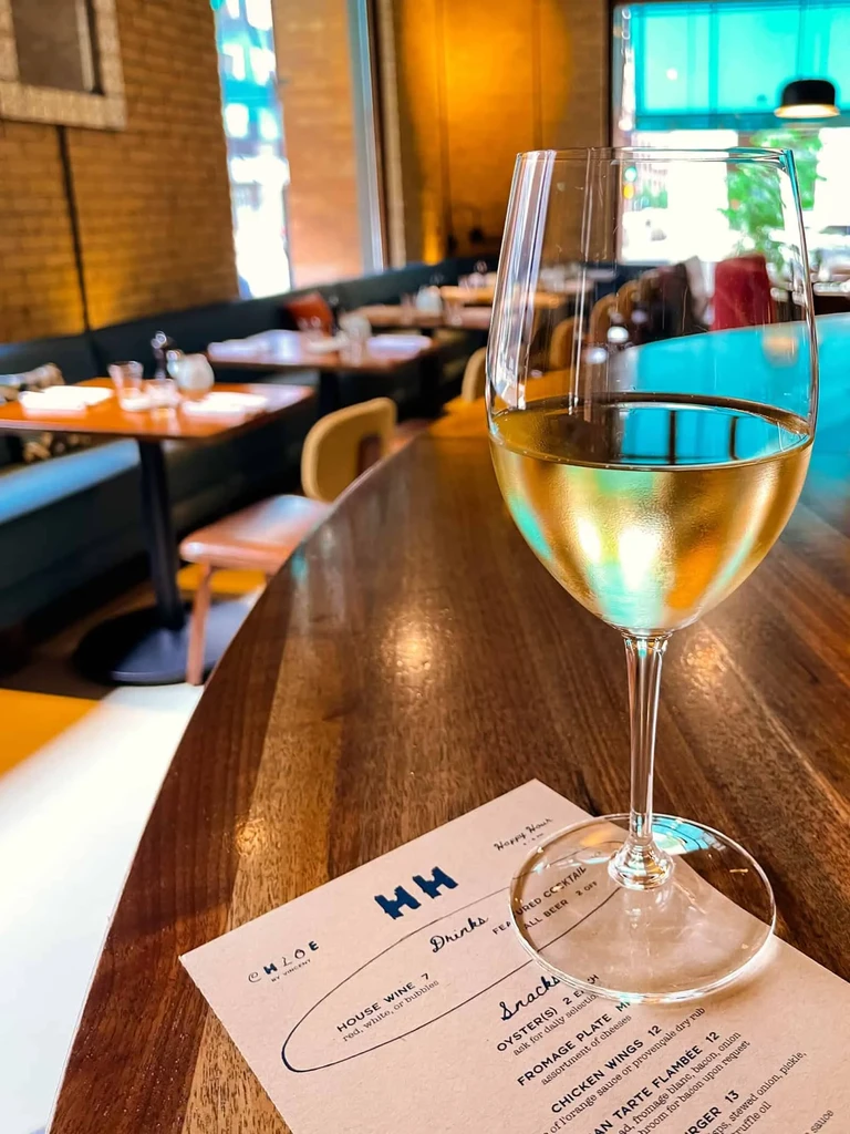 Glass of white wine on wooden table, menu visible.