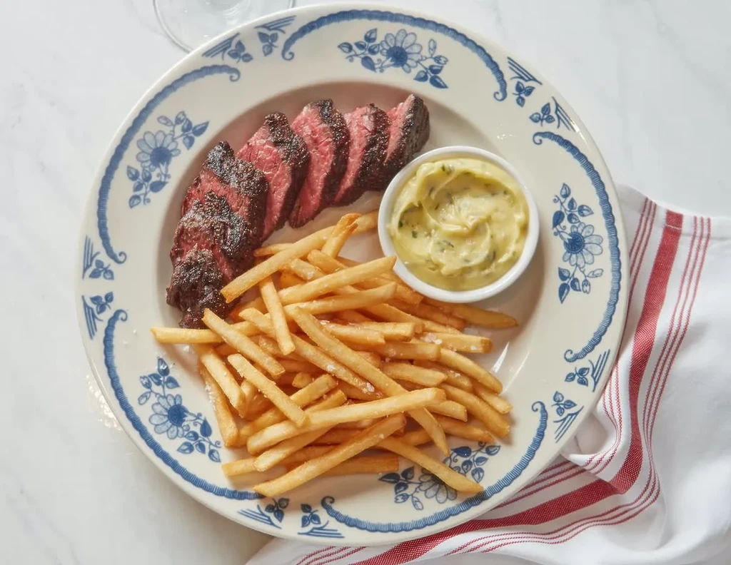 Medium-rare sliced steak, golden fries, and herb sauce on a floral plate.