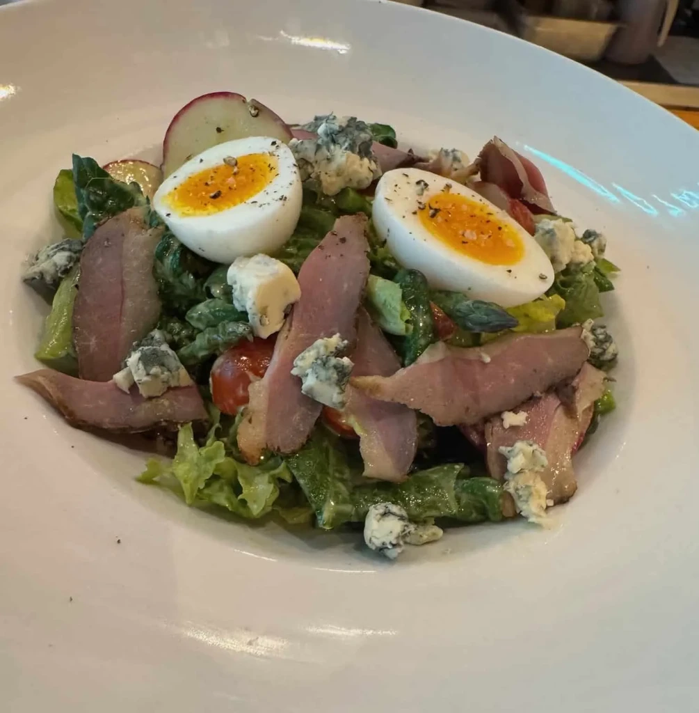 Close-up of a colorful salad with meat, cheese, eggs, and vegetables.